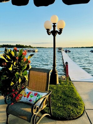 A bench with a cushion, a lamp post, and a view of a body of water with boats.