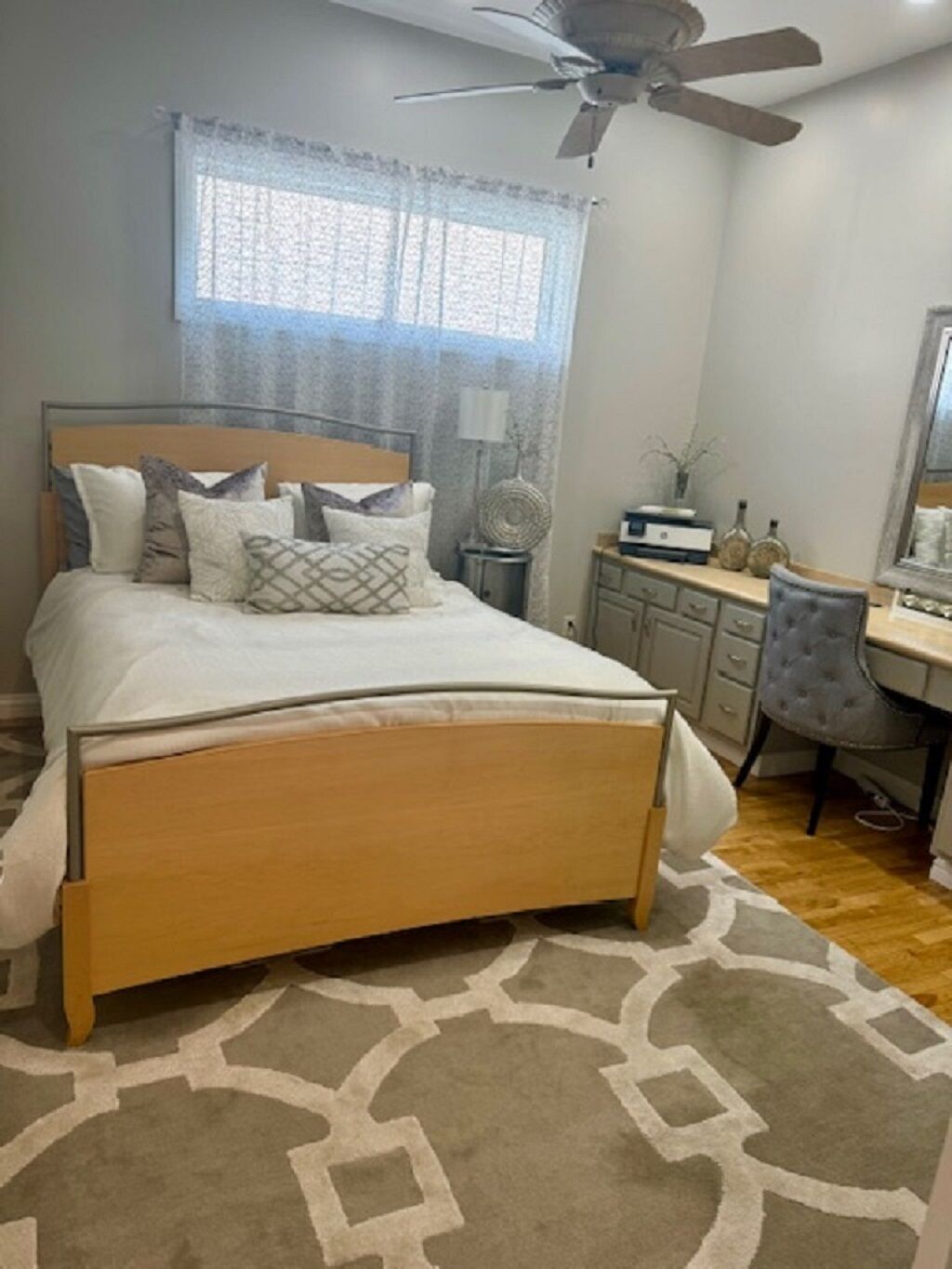 A bedroom with a bed, a desk, a chair, a ceiling fan, and a window with curtains.