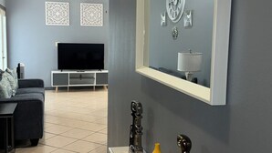 Un saló amb una paret gris, un mirall gran, televisió de pantalla plana, un sofà i objectes decoratius sobre una taula consola.