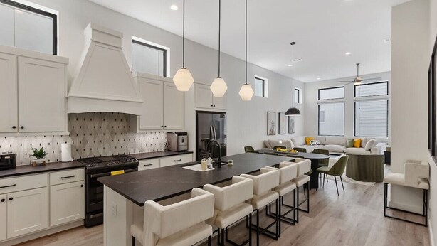 Une cuisine moderne avec des meubles blancs, un îlot central doté de tabourets, un éclairage suspendu et un coin repas avec une table et des chaises.
