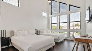 Une chambre avec deux lits, un bureau et de grandes fenêtres.
