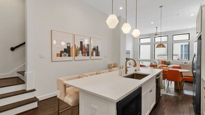 Une cuisine moderne dotée d’un îlot central, d’un four encastré et de luminaires suspendus.