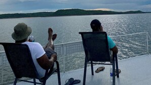 Two people seated on chairs facing a body of water with a hilly landscape in the distance. - BaTonga Villa (Binga)