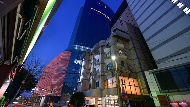 Une rue moderne en milieu urbain, avec un immeuble imposant à façade vitrée et un bâtiment traditionnel à la façade incurvée.