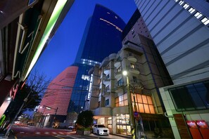 A modern urban street with a prominent glass building and a traditional building with a curved facade. - Morning Calm (Jeju City)
