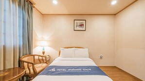 Une chambre d’hôtel avec un lit, une chaise, une table, une lampe et un tableau encadré au mur.