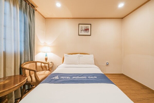 Una habitación de hotel con cama, una silla, una mesa, una lámpara y un cuadro en la pared.