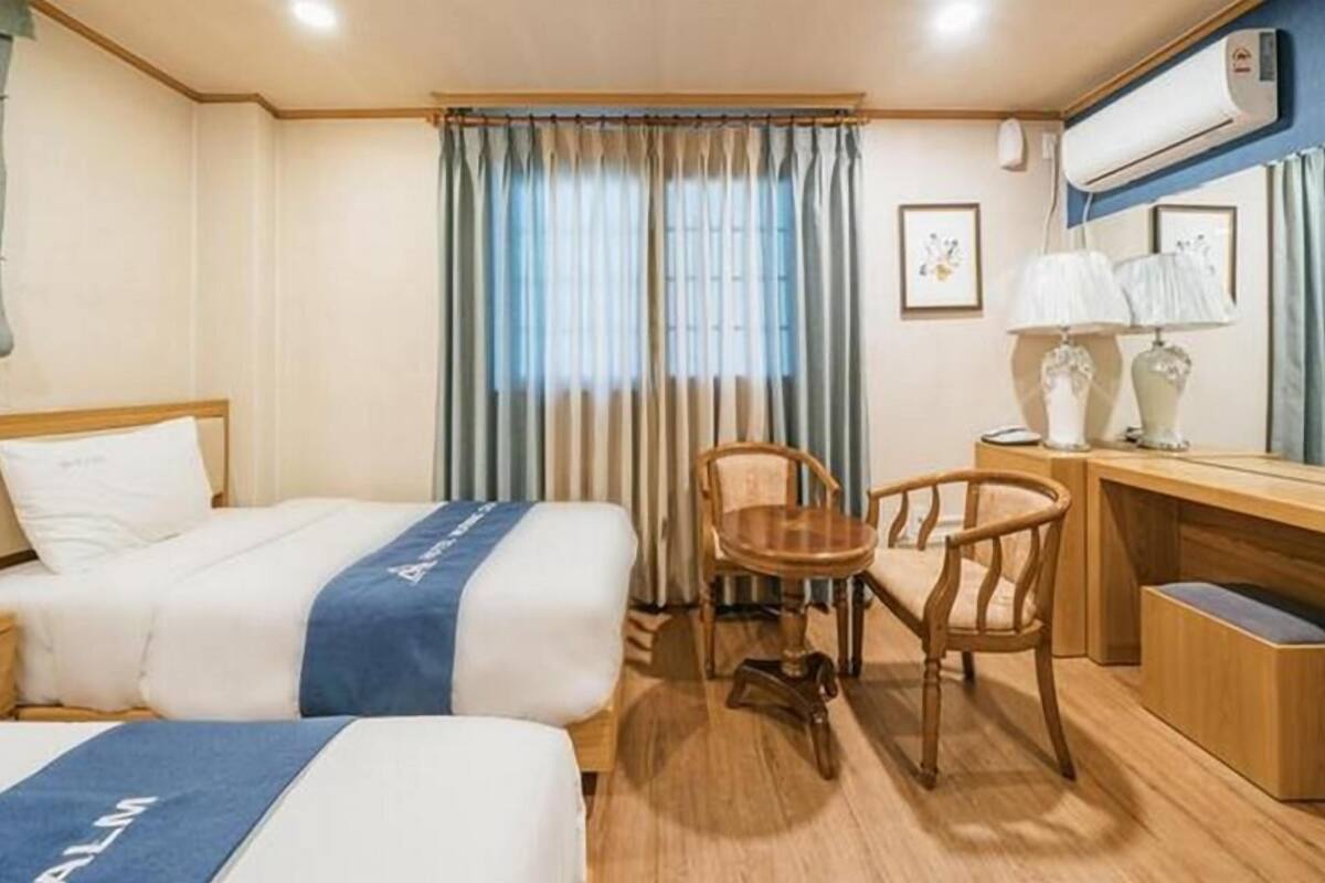 A hotel room with two beds, a desk, a chair, and a window with curtains.