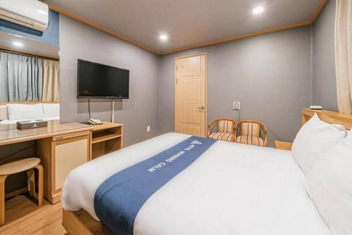 A hotel room with a bed, a desk, a chair, a television, and a door.