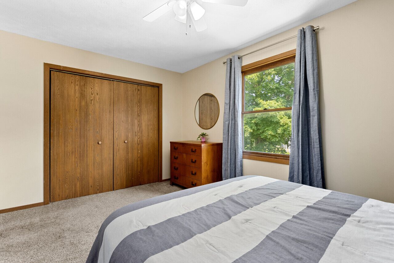 Ein Schlafzimmer mit Bett, Holzschrank, Schminktisch, Spiegel und einem Fenster mit Vorhängen.