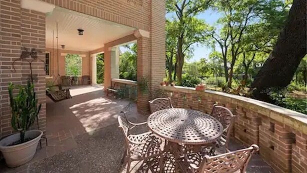 A covered patio area with a brick wall, outdoor seating, and a view of trees. - Majestic Hyde Park Historic Home (Austin)