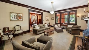 A spacious living room with a fireplace, multiple seating options, and large windows providing natural light. - Majestic Hyde Park Historic Home (Austin)