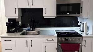 Ett modernt kök med vita skåp, en svart mikrovågsugn, en spis i rostfritt stål och en inbyggd ugn.