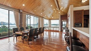 Un comedor amplio con una mesa y sillas de madera, ventanas grandes con vistas a la ciudad y al agua, y una cocina moderna con microondas.