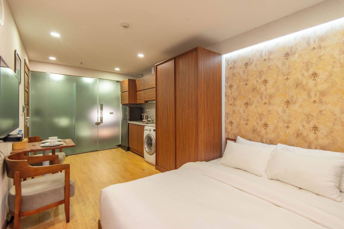 A compact hotel room with a bed, a small kitchenette, a washing machine, and a dining area.