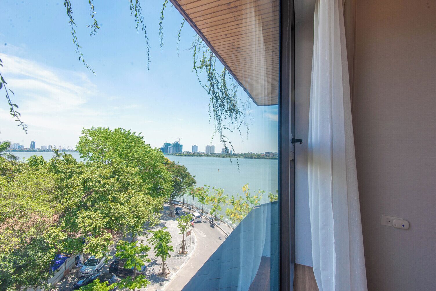A balcony with a view of a waterfront, trees, and parked cars.
