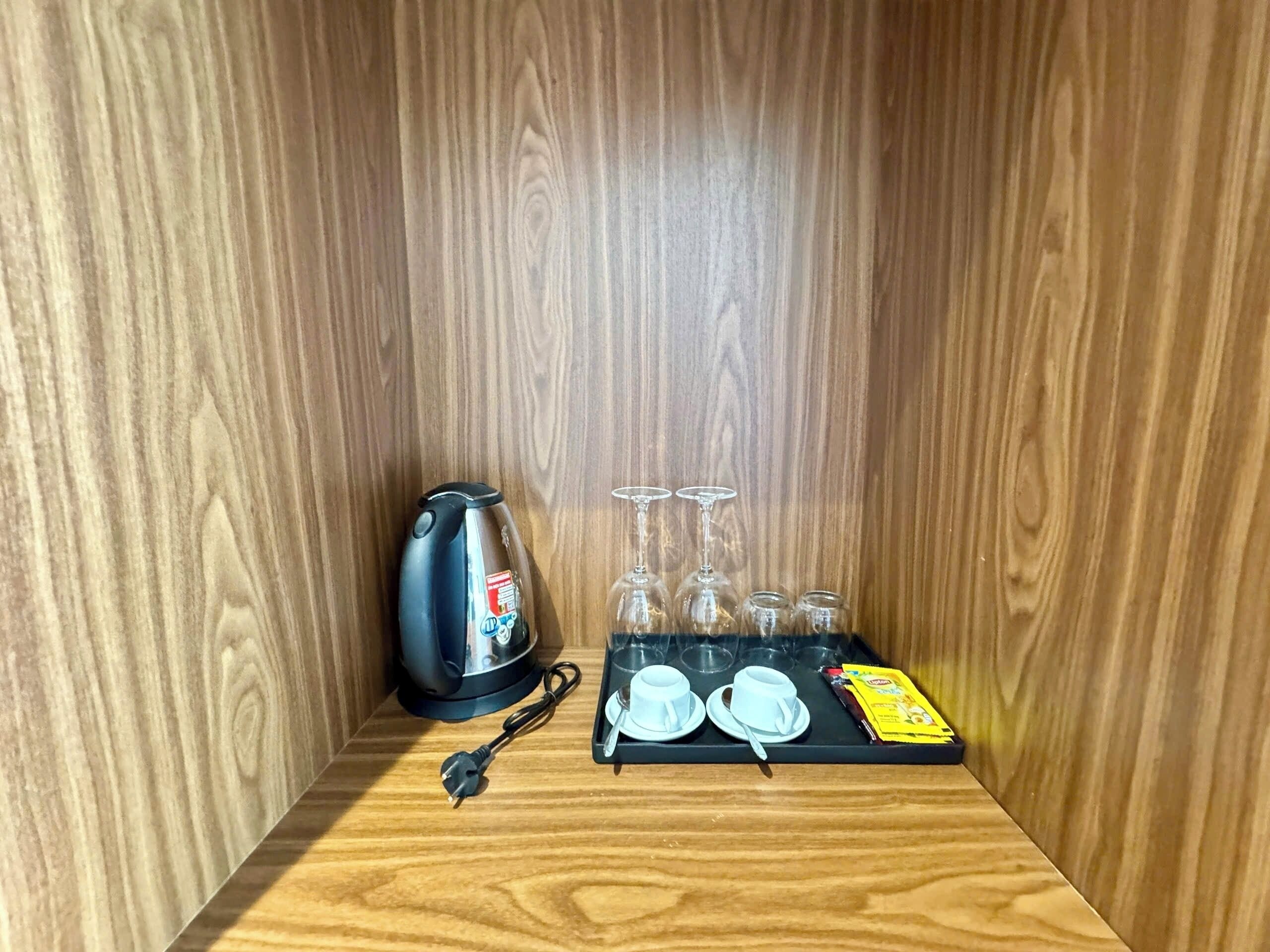 A wooden cabinet with a kettle, cups, and a tea packet.
