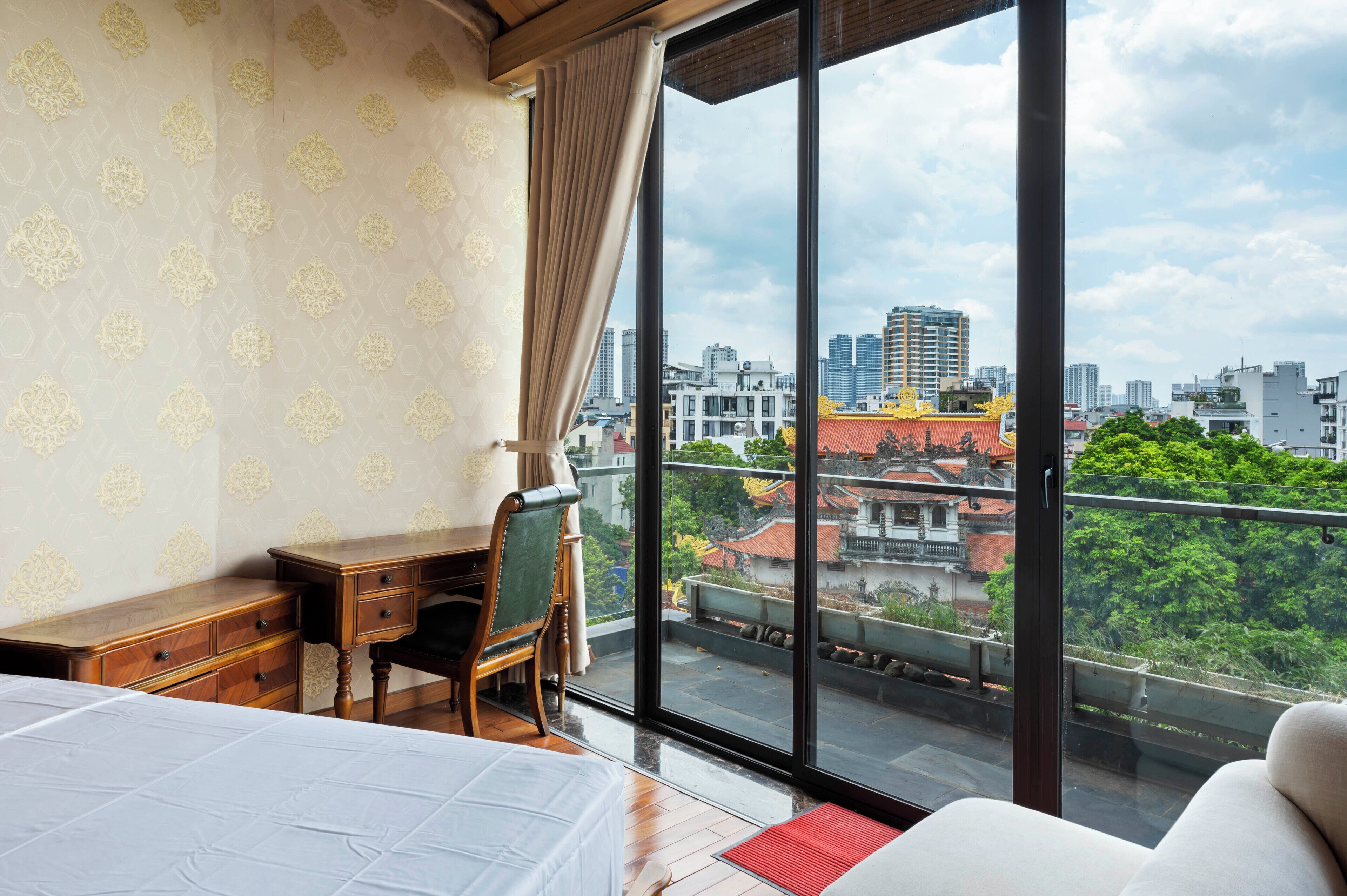 A bedroom with a large window, a wooden desk, a chair, and a bed.