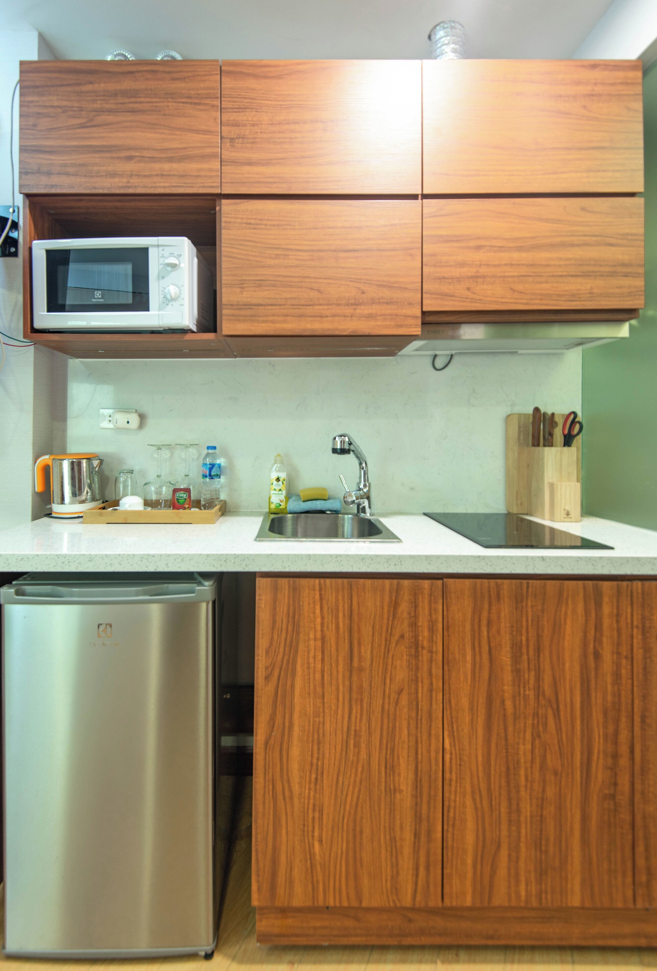 A compact kitchen with wooden cabinets, a stainless steel dishwasher, a microwave, and a sink.