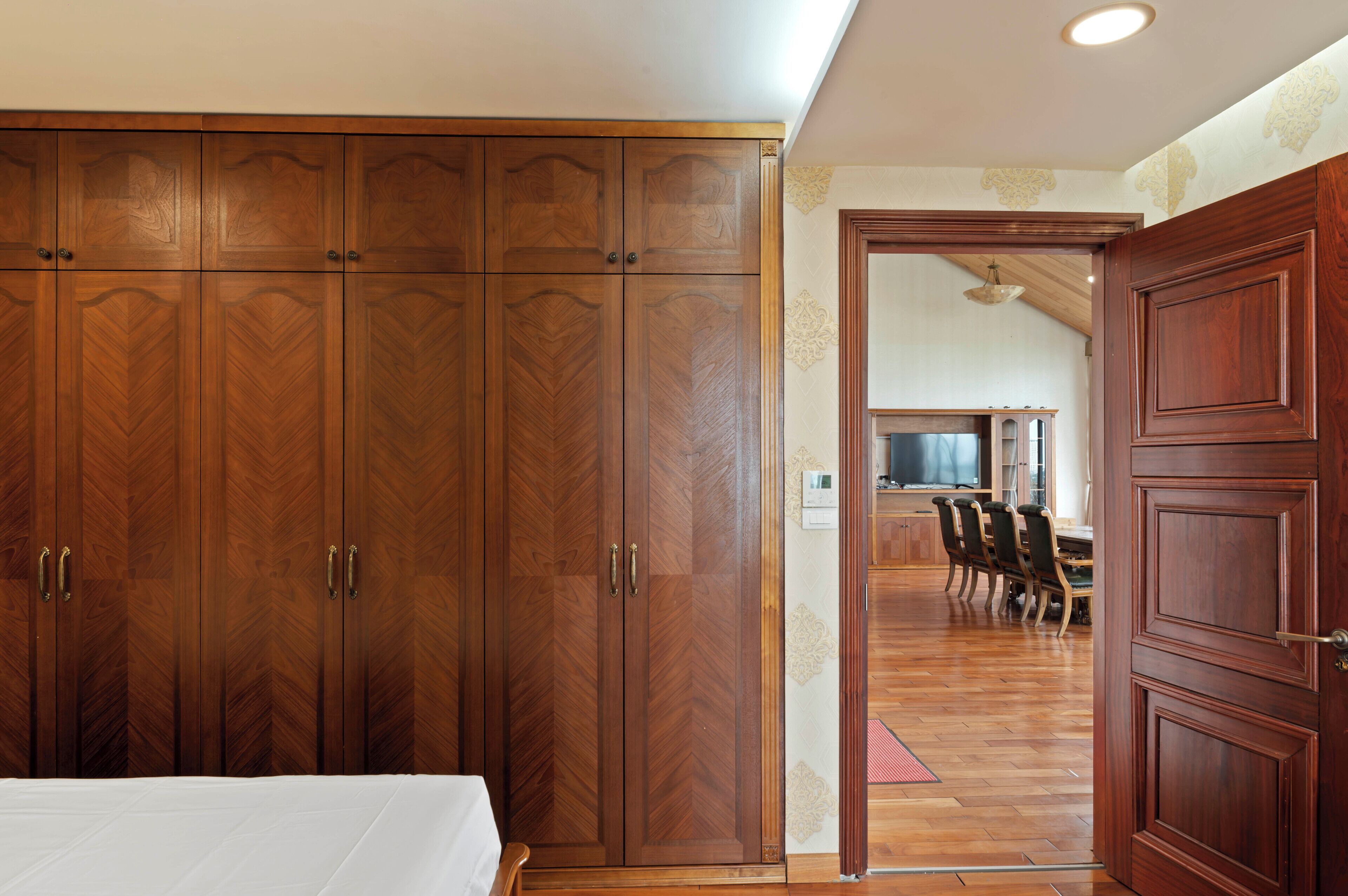 A bedroom with a large wardrobe, a bed, and a dining area with chairs and a table.