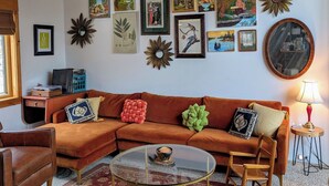 A cozy living room with a wooden ceiling, a sectional sofa, a glass coffee table, and various wall art. - Shambhala Mountain Retreat: A chalet surrounded by forest. Relax & unwind! (Napanoch)
