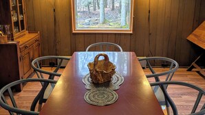 A dining area with a wooden table, chairs, a wooden cabinet, and a window with a forest view. - Shambhala Mountain Retreat: A chalet surrounded by forest. Relax & unwind! (Napanoch)