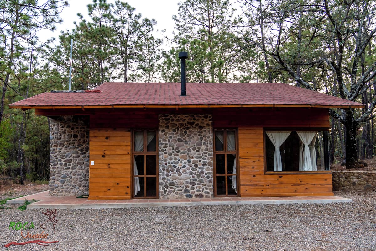 A cabin with a stone facade, wooden exterior, and a red-tiled roof.