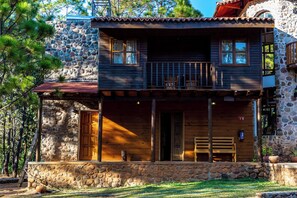 A two-story stone cabin with a wooden balcony, a front porch, and a stone wall.