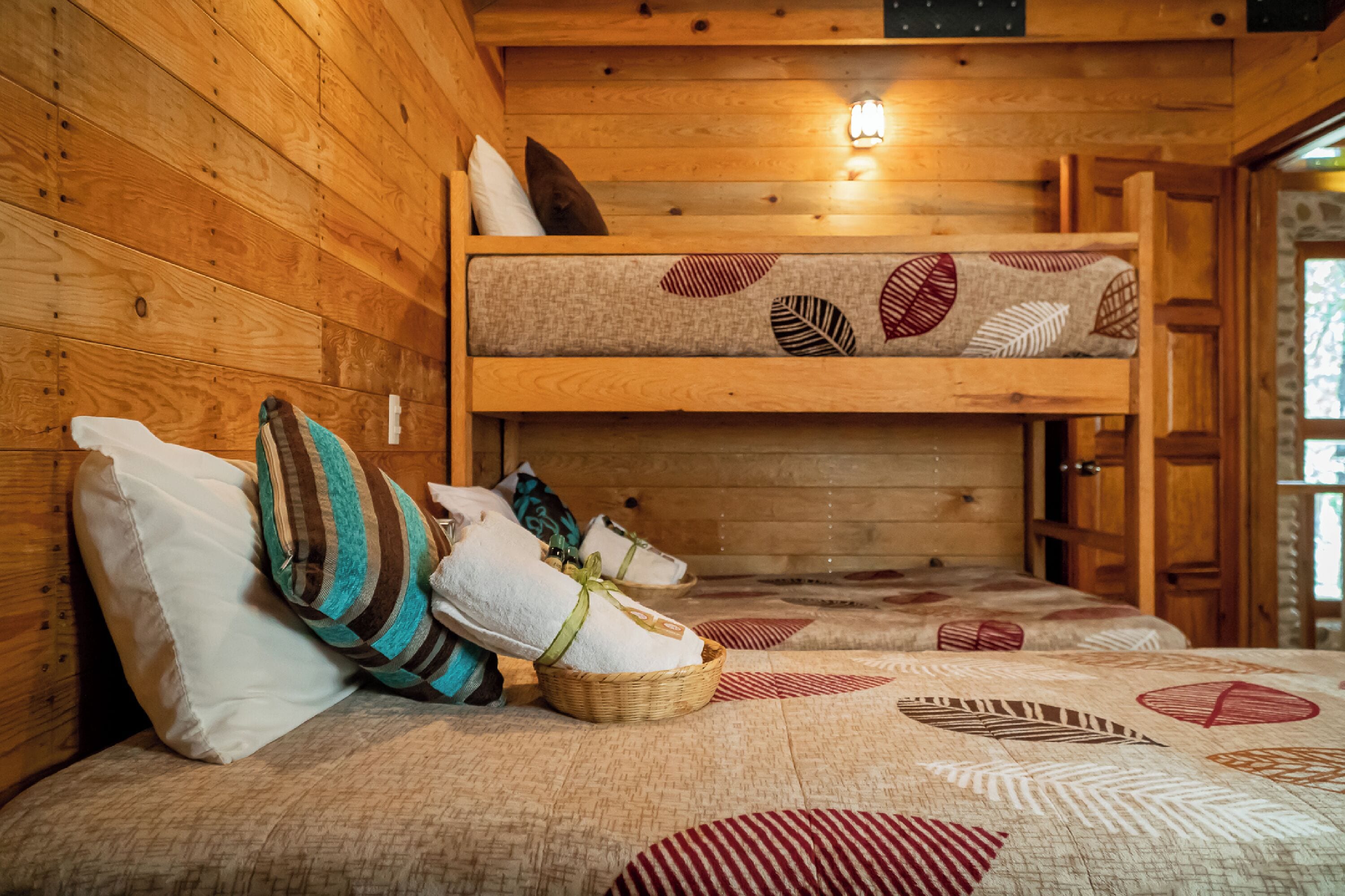 L’intérieur d’un chalet en bois, avec un lit superposé, des oreillers et une courtepointe ornée de motifs de feuilles.