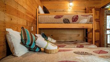 L’intérieur d’un chalet en bois, avec un lit superposé, des oreillers et une courtepointe ornée de motifs de feuilles.