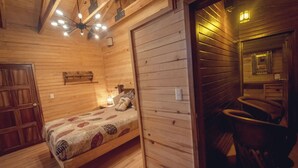 A wooden cabin room with a bed, a bench, a small table, and a mirror. - Roca Venados (Mascota)