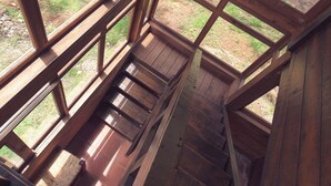 A wooden staircase leading to a loft area with large windows offering a view of a forested area. - Roca Venados (Mascota)