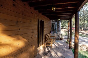 A wooden cabin with a porch, a bench, and a stone wall.