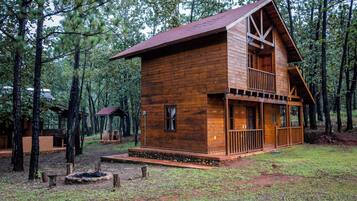 A wooden cabin with a balcony, surrounded by trees.