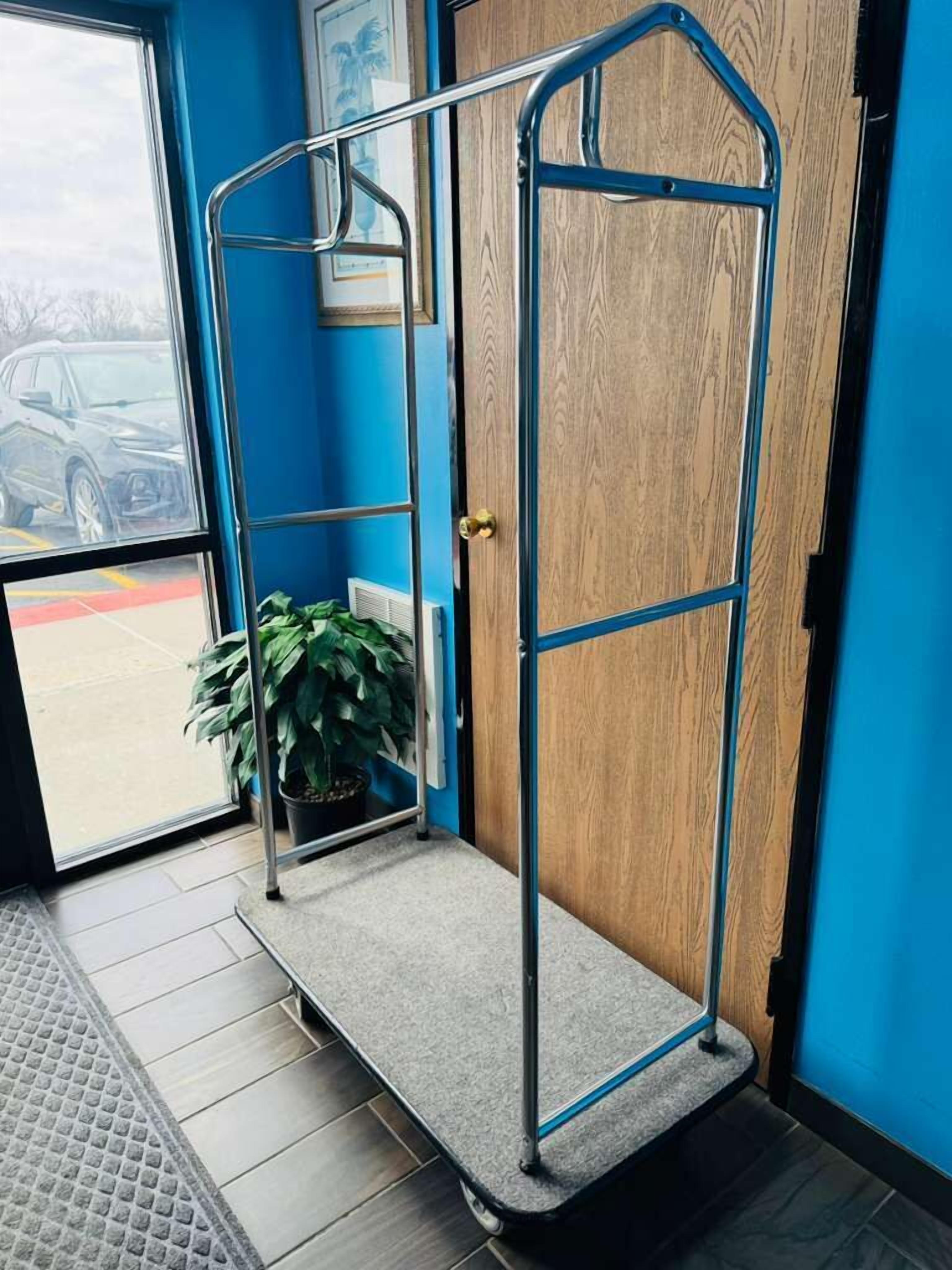 Una habitación con pared azul, puerta de madera, carro metálico y planta en maceta.