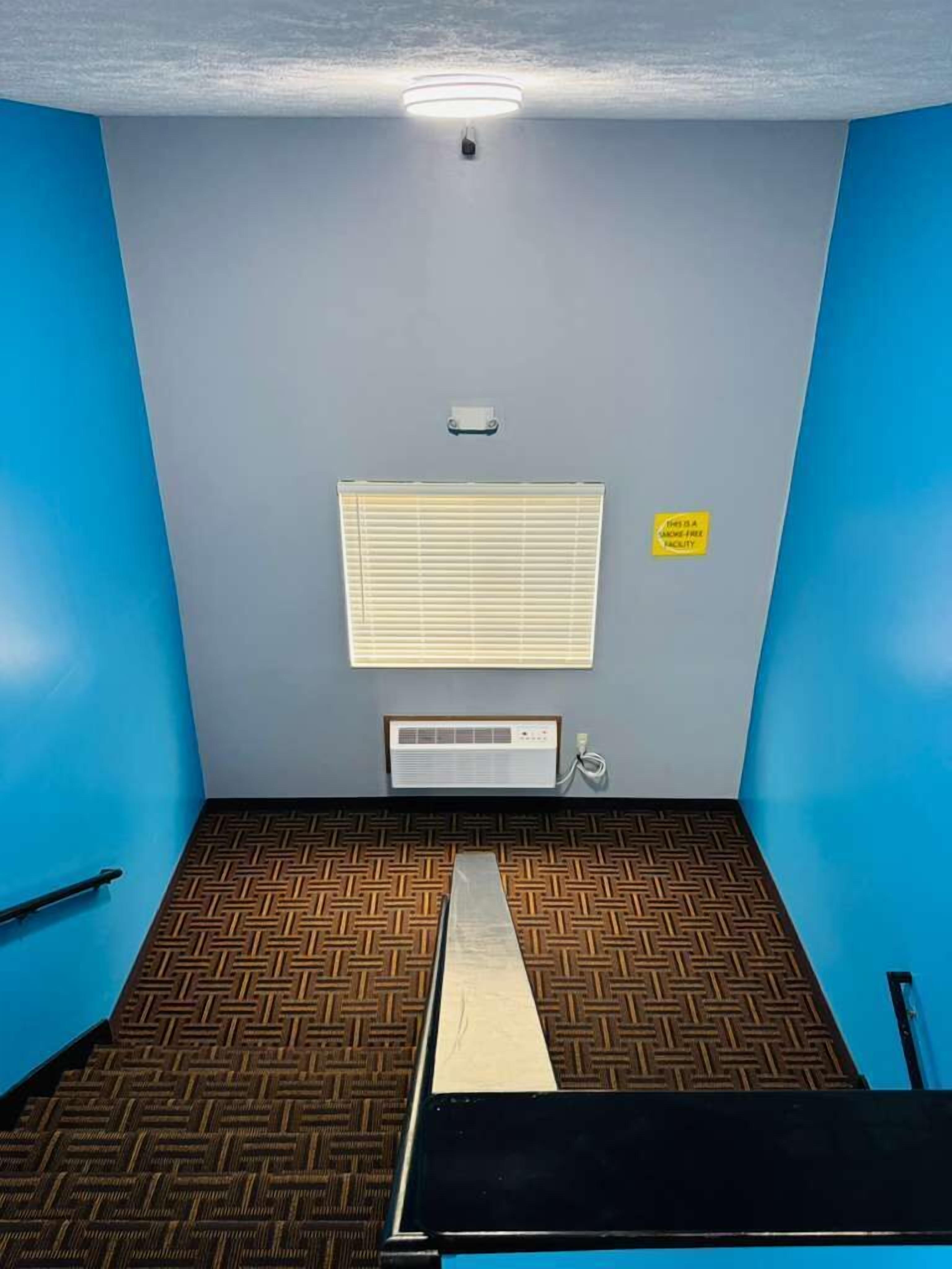 Een kamer met een patroon vloer, een plafondlamp, een raam met zonwering en een bord dat een rookvrije faciliteit aangeeft.