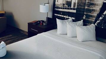 A hotel room with a large bed, a nightstand with a lamp, a clock, and a poster on the wall.