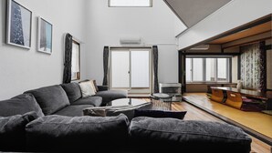A modern living room with a grey sofa, a coffee table, and a dining area with a wooden table and chairs. - THE BEEHIVE 1 (Sapporo)