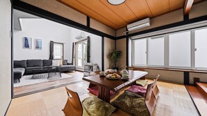 A traditional Japanese-style room with tatami flooring, a low wooden table set for dining, a sofa, and a view of the outside through large windows. - THE BEEHIVE 1 (Sapporo)