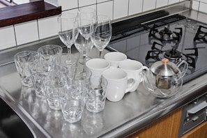 Un comptoir de cuisine avec divers articles en verre, notamment des verres à vin et des tasses, ainsi qu’une cuisinière à gaz avec des brûleurs.