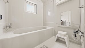 A modern bathroom with a freestanding bathtub, a small sink, a window, and a mirror. - THE BEEHIVE 1 (Sapporo)