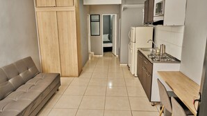 Une cuisine compacte comprenant un canapé, des placards, une cuisinière et un four à micro-ondes.