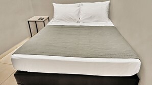 Un lit simple avec une couette grise, des oreillers blancs et un pied de lit noir.