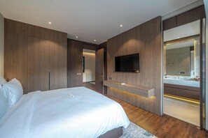 A modern bedroom with a large bed, built-in TV, and a bathroom with a large mirror.
