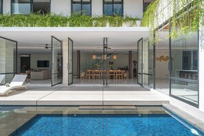 A modern outdoor pool area with a glass-enclosed dining space and lounge chairs.