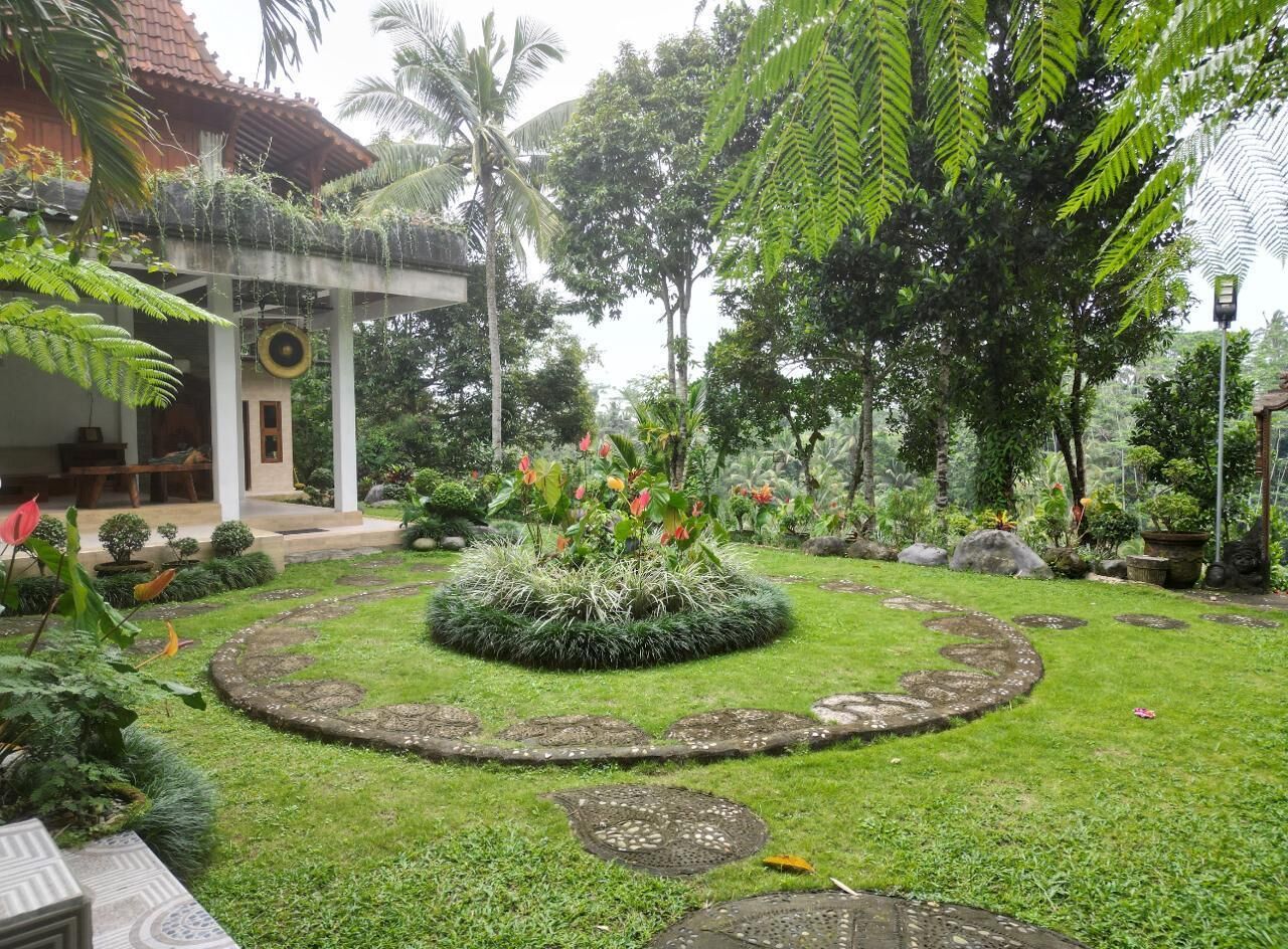 A well-maintained garden with a circular flower bed, palm trees, and a traditional building with a tiled roof.
