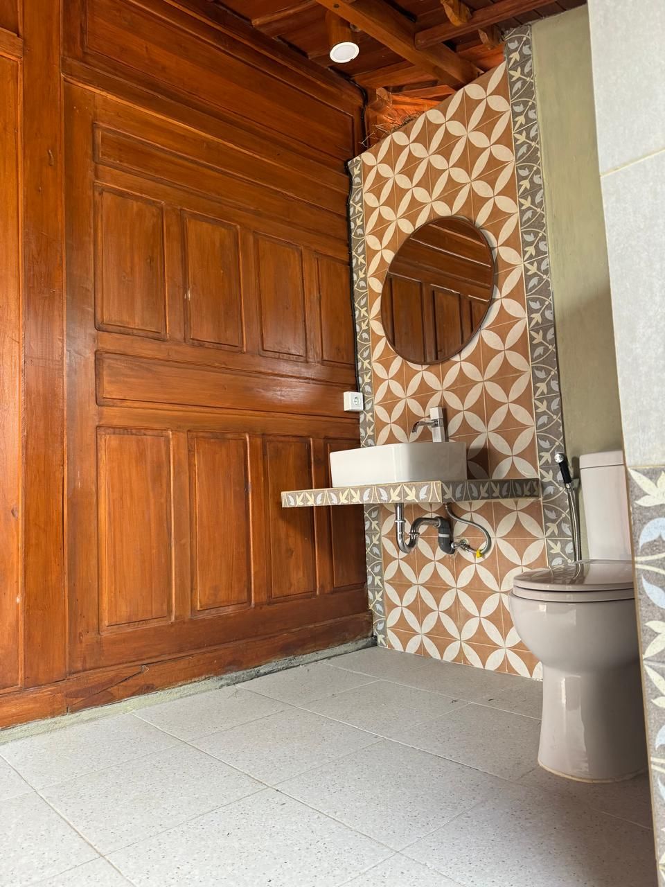 A bathroom with a wooden door, a sink with a mirror, and a toilet.