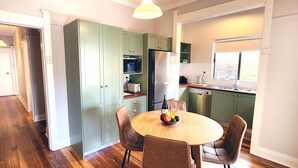 Une cuisine moderne avec des meubles de couleur verte, un réfrigérateur en acier inoxydable et un coin repas comprenant une table en bois et des chaises en cuir.