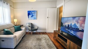 Un salon avec un canapé, un fauteuil, un téléviseur et un tableau accroché au mur.