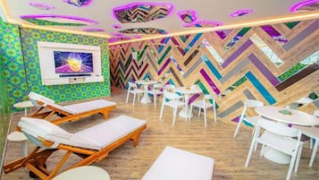 A modern lounge area with wooden flooring, white lounge chairs, and tables.
